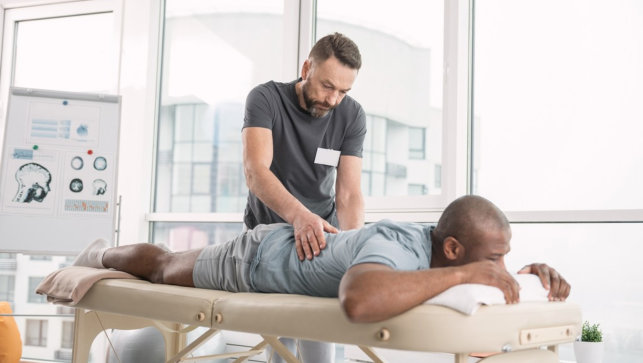 Skillful orthopedist. Skilled bearded man doing a back massage for his patient while working as an orthopedist